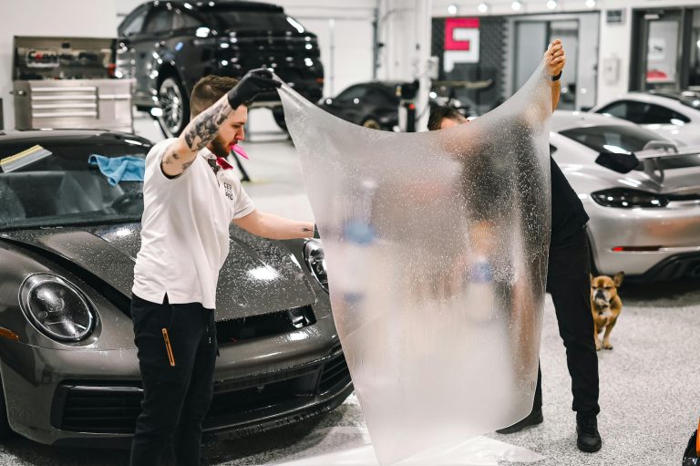 Two professionals applying protective film to a luxury car in a modern garage.